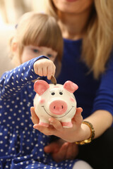 Child little girl arm putting coins into piggybank