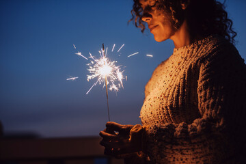 Adult woman with closed eyes holding sparkler in the night with blue sky in background - new year eve christmas holidays - female people with firework outdoor enjoy emotions and feeling