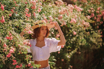 Outdoor summer portrait of young beautiful woman wearing trendy  straw hat, vintage style white blouse, posing in blooming garden. Copy, empty space for text
