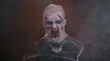 Sinister scary man in carnival costume of Halloween crazy zombie with bloody wounded scars face trying to scare isolated on black room. Horror theme of cosplay wounded undead, beast, monster
