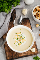 Wall Mural - Homemade cauliflower soup puree in a white bowl with cheese, cream, spices and fresh parsley on a gray concrete background. Top view, copy space.