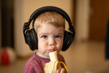 Niño rubio comiendo banana escuchando música con auriculares