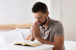 © New Africa - Religious man with Bible praying in bedroom