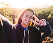 © ADDICTIVE STOCK - Smiling teenager showing peace gesture while taking selfie against mountain