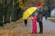 © somemeans - Small child stands in the yellow rain next to his mother in the park against the background of autumn yellow foliage