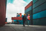 Industrial worker works with co-worker at overseas shipping container yard . Logistics supply chain management and international goods export concept .