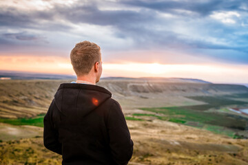 Wall Mural - A young man conquered the top of the mountain at dawn. Beautiful mountain landscape with a slope. The concept of enjoying nature.