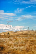 Power Lines In A Dry Yellow Field Against A Blue Sky With Clouds
