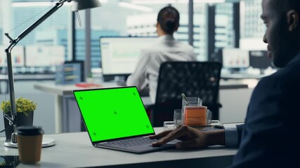 Leinwandbilder - Successful Black Businessman Sitting at Desk Working on Green Screen Laptop Computer in Office. Handsome African American Businessperson using Chroma Key Display. Over Shoulder