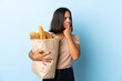 Young latin woman buying some breads isolated on blue background nervous and scared