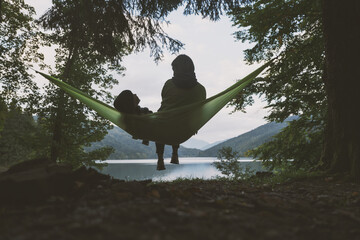 Small kid with mother on hammock on forest lake background. Childhood with nature loving concept