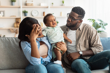 Wall Mural - Tired black parents sitting with crying kid on sofa