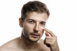 © blackday - Men's beauty. Young man is applying moisturizing and anti aging cream on his face