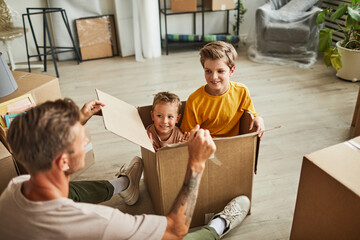 Wall Mural - Portrait of happy father playing with two boys in cardboard boxes while family moving to new house, copy space