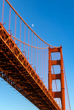 Closeup Of Portion Of Golden Gate Bridge In San Francisco, California, With Glowing Crescent Slivered Moon And Deep Blue Twilight Sky.