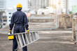© zephyr_p - Asian maintenance worker man with protective suit and safety helmet carrying aluminium step ladder and tool box at construction site. Civil engineering, Architecture builder and building service