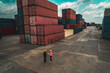 © InfiniteFlow - Industrial worker works with co-worker at overseas shipping container yard . Logistics supply chain management and international goods export concept .