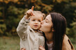 © Ananass - Young happy and smiling mom with her little daughter in arms hugging and kissing spending a weekend on a walk in autumn park. selective focus, noise effect, Autumnal mood