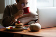 © Kashper - Young woman working on the laptop and drinking coffee at home