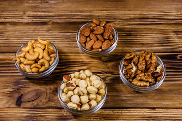 Poster - Various nuts (almond, cashew, hazelnut, walnut) in glass bowls on a wooden table. Vegetarian meal. Healthy eating concept