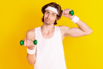 Portrait of attractive weak clueless sportive guy lifting weight isolated over bright yellow color background