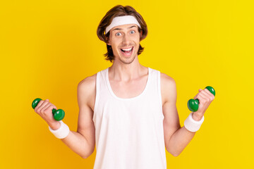 Sticker - Portrait of attractive cheerful sportive clueless guy lifting dumbbell isolated over bright yellow color background