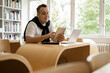 © muse studio - A student at a desk studying at a college. A young man in the library of the Institute. Read an online book on a computer. A new academic year at the university.