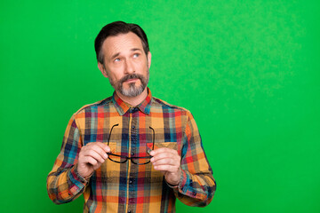 Poster - Portrait of attractive bewildered man holding in hands specs thinking copy space isolated over bright green color background