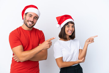 Wall Mural - Young couple with christmas hat isolated on white background pointing finger to the side in lateral position