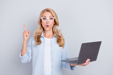 Sticker - Portrait of shocked amazed mature businesswoman advertise product hold laptop wear glasses isolated on grey color background