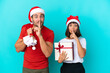 © luismolinero - Young couple with christmas hat handing out gifts isolated on blue background showing a sign of silence gesture putting finger in mouth
