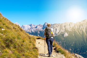 Wall Mural - Woman hiking a trail in the Italian alps at the end of summer or fall. Dolomite peaks of Rosengarten - Catinaccio are visible in the background. Carezza, Val d'Ega - Trentino, Italy