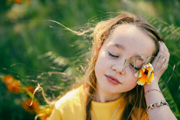 Wall Mural - Portrait of pretty girl sitting in field with vibrant orange and yellow wildflowers