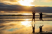 A Family Of Two Jumping For Joy In Cannon  Beach During Sunset.