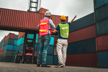 Industrial worker works with co-worker at overseas shipping container yard . Logistics supply chain management and international goods export concept .