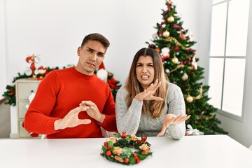 Poster - Young hispanic couple sitting at the table on christmas disgusted expression, displeased and fearful doing disgust face because aversion reaction. with hands raised