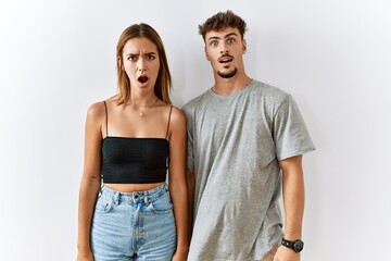 Poster - Young beautiful couple standing together over isolated background in shock face, looking skeptical and sarcastic, surprised with open mouth