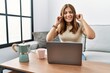 © Krakenimages.com - Young brunette woman using laptop at home drinking a cup of coffee covering ears with fingers with annoyed expression for the noise of loud music. deaf concept.