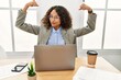 © Krakenimages.com - Beautiful hispanic business woman sitting on desk at office working with laptop showing arms muscles smiling proud. fitness concept.
