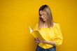 © Volodymyr - Beautiful smart young girl holding and reading book isolated on the yellow background. Portrait of attractive woman in a yellow blouse and wearing glasses reading book. Education, studying, knowledge.