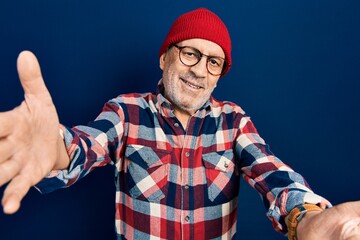 Wall Mural - Handsome mature man wearing hipster look with wool cap looking at the camera smiling with open arms for hug. cheerful expression embracing happiness.