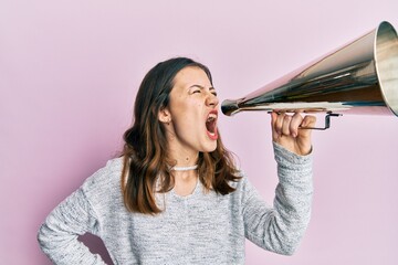 Wall Mural - Young brunette woman shouting and screaming through vintage megaphone over pink isolated background