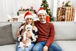 © Krakenimages.com - Young couple of wife and husband sitting on the sofa wearing christmas hat at home looking positive and happy standing and smiling with a confident smile showing teeth