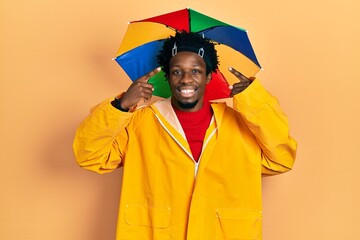 Sticker - Young african american man wearing yellow raincoat smiling pointing to head with both hands finger, great idea or thought, good memory