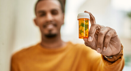 Wall Mural - Young african american man smiling happy holding pills at the city.