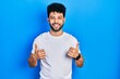 © Krakenimages.com - Young arab man with beard wearing casual white t shirt success sign doing positive gesture with hand, thumbs up smiling and happy. cheerful expression and winner gesture.