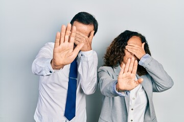 Poster - Middle age couple of hispanic woman and man wearing business office uniform covering eyes with hands and doing stop gesture with sad and fear expression. embarrassed and negative concept.