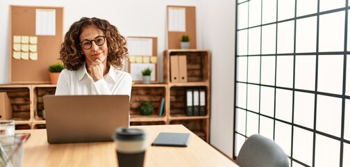 Canvas Print - Middle age hispanic woman working at the office wearing glasses looking confident at the camera smiling with crossed arms and hand raised on chin. thinking positive.