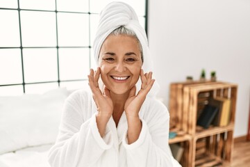 Sticker - Middle age grey-haired woman using face cream sitting on the bed at bedroom.