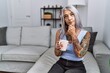 © Krakenimages.com - Middle age grey-haired woman drinking coffee sitting on the sofa at home looking confident at the camera smiling with crossed arms and hand raised on chin. thinking positive.